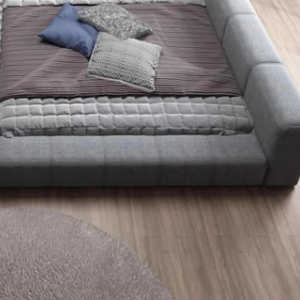 Modern grey fabric double bed with a low-profile padded frame, dressed with a purple quilt and decorative cushions.