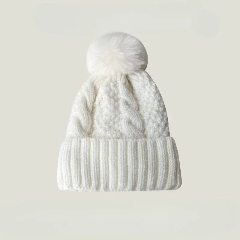 White cable-knit beanie hat featuring a fluffy faux fur pom-pom and a ribbed turn-up cuff.