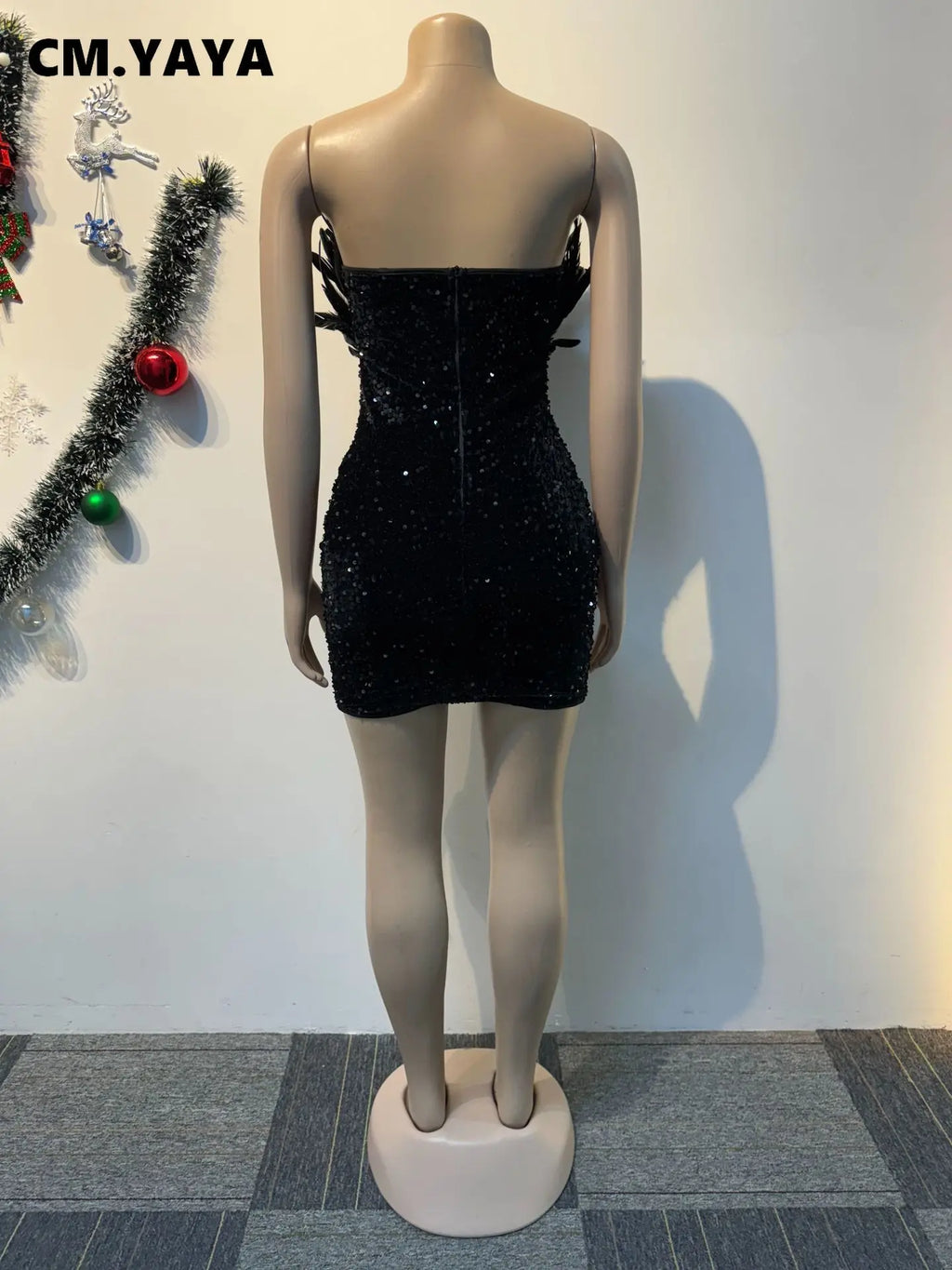 Back view of a black strapless sequined bodycon mini dress on a mannequin with feather accents.