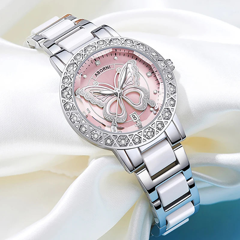 Luxury women's watch with a pink dial, butterfly motif, crystal-set bezel, and a white and silver-tone metal strap.