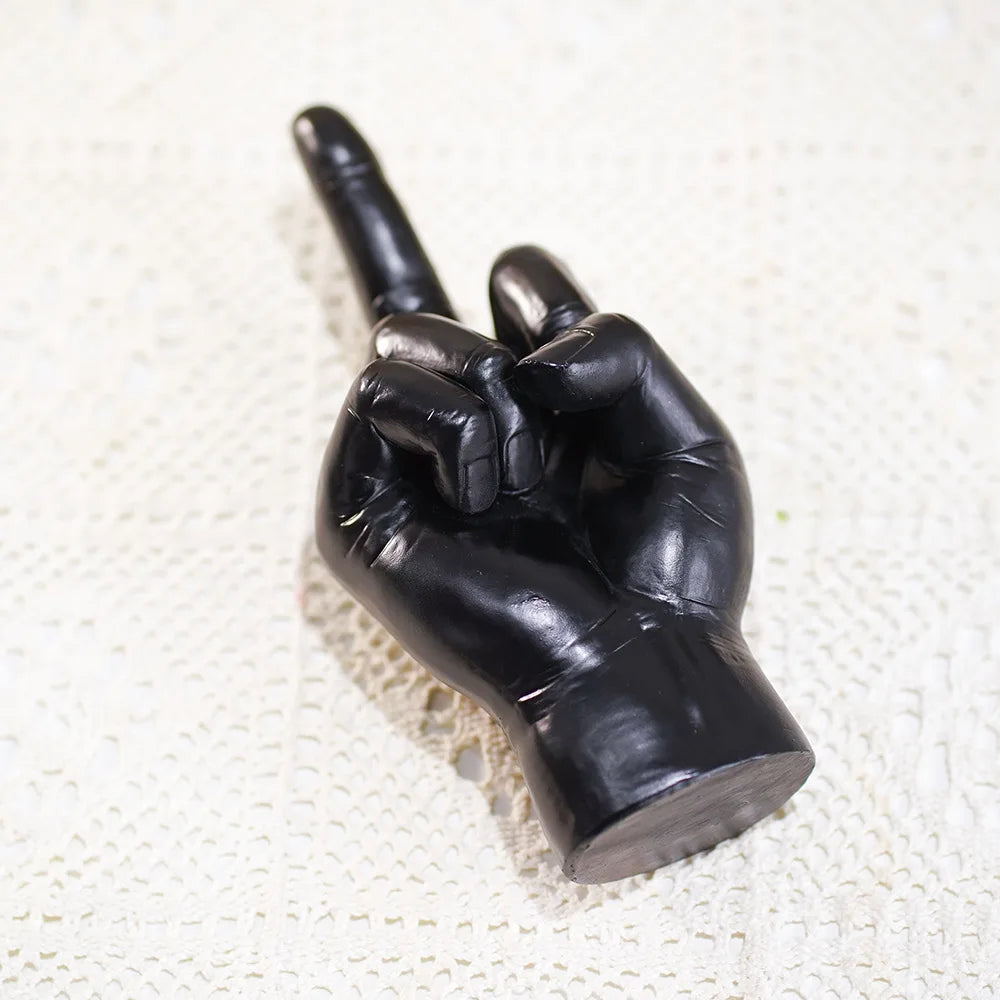 Glossy black resin sculpture of a hand gesturing with a raised index finger, on a cream lace background.