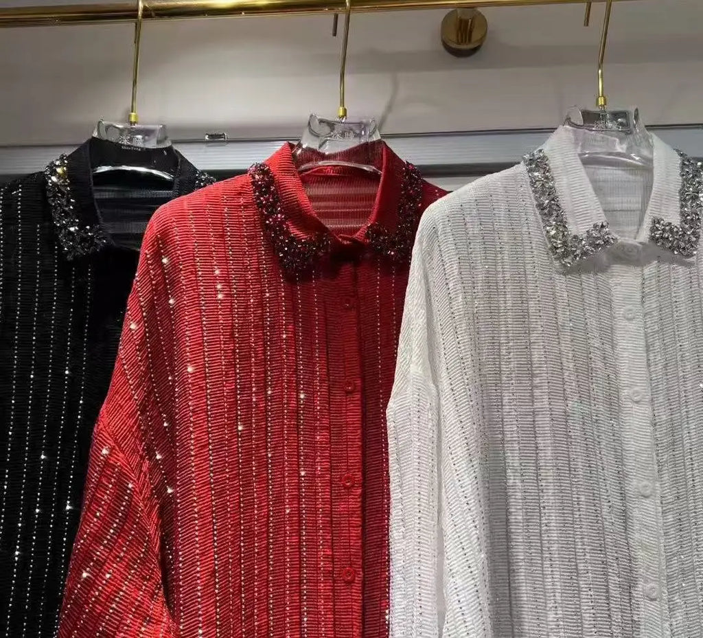 Three long-sleeve, pleated shirts in black, red, and white, each featuring a crystal-embellished collar and button front.