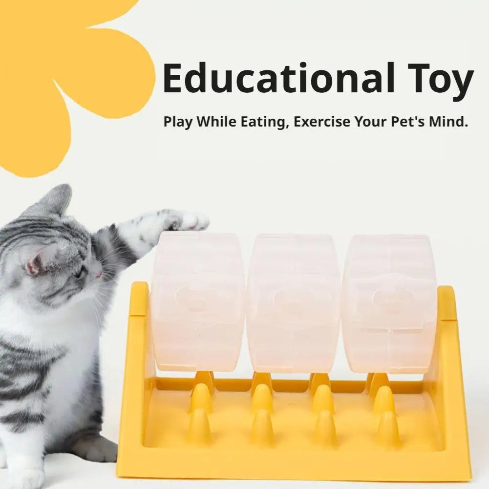 A tabby cat paws at a yellow interactive feeder with three clear, rotating treat-dispensing cylinders.
