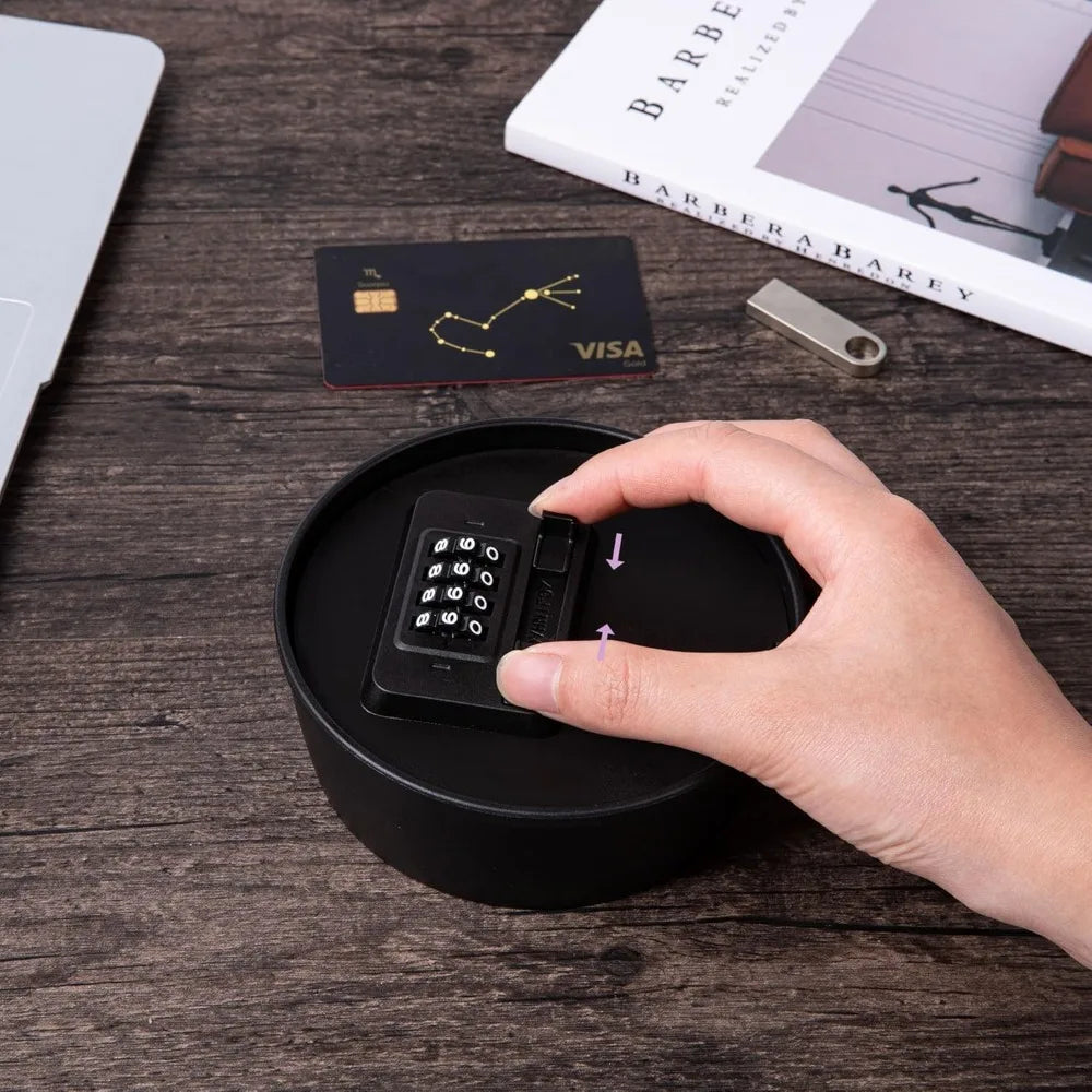 A black, circular metal safe with a push-button digital combination lock being opened by a hand.