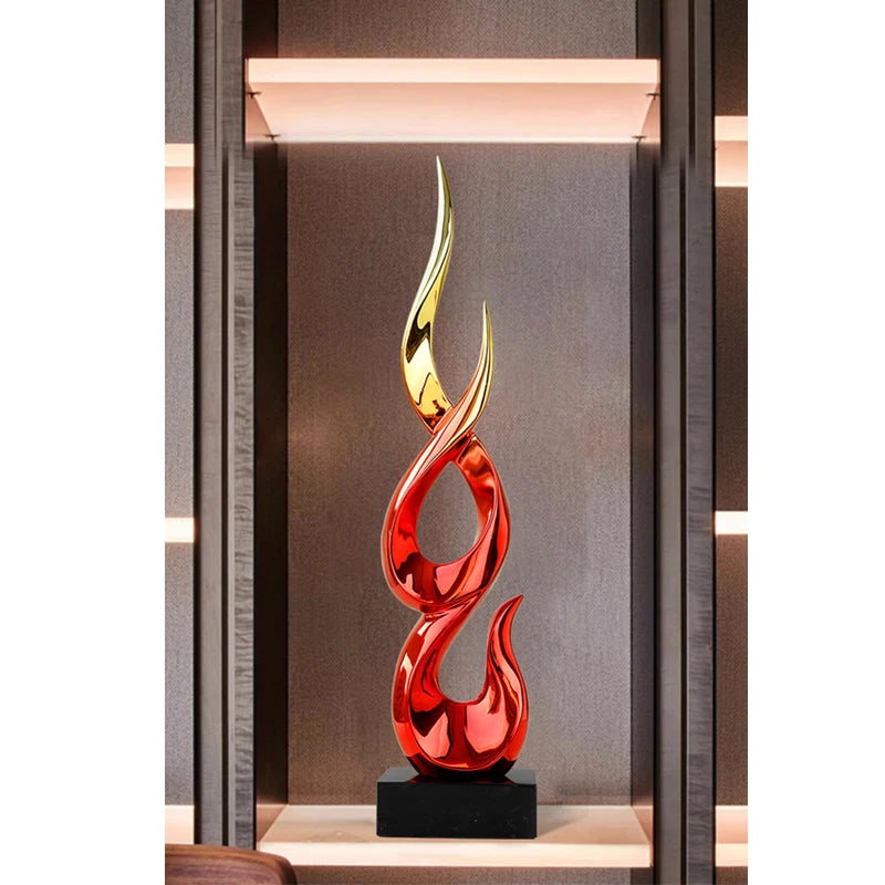 Modern abstract flame sculpture with a glossy red and gold finish, mounted on a sleek black base.