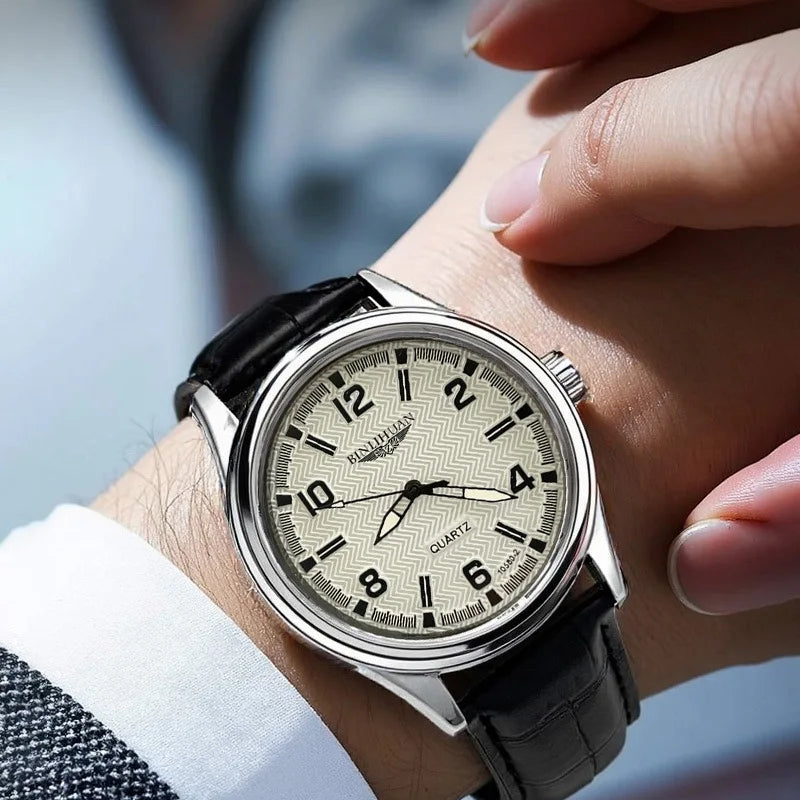 Classic men’s quartz watch with a silver case, textured beige face, and black leather strap worn on the wrist.