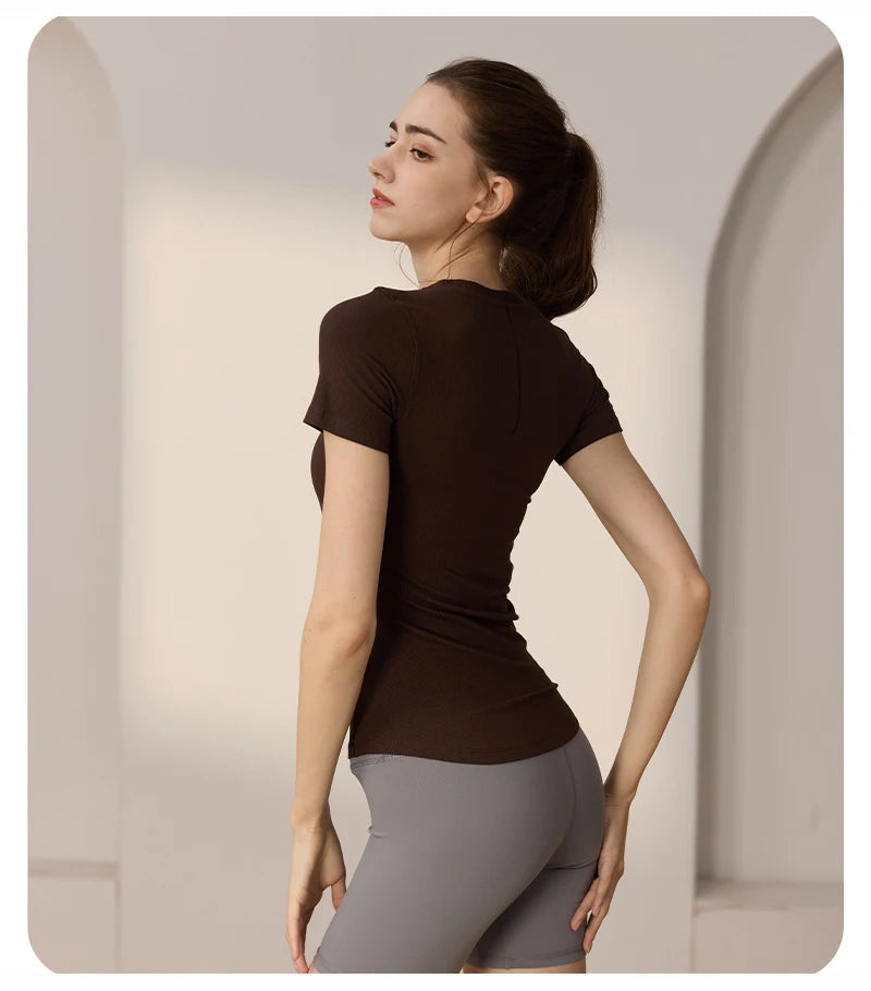 Model wearing a dark brown, short-sleeved, ribbed slim-fit workout top paired with grey cycling shorts.