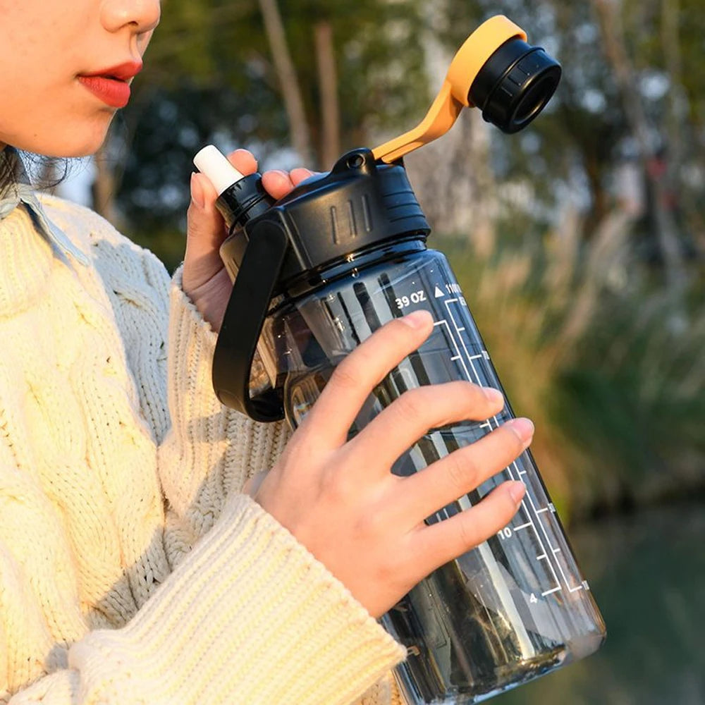 Large black water bottle with a yellow carry loop, clear design, and measurement markings held by a person.