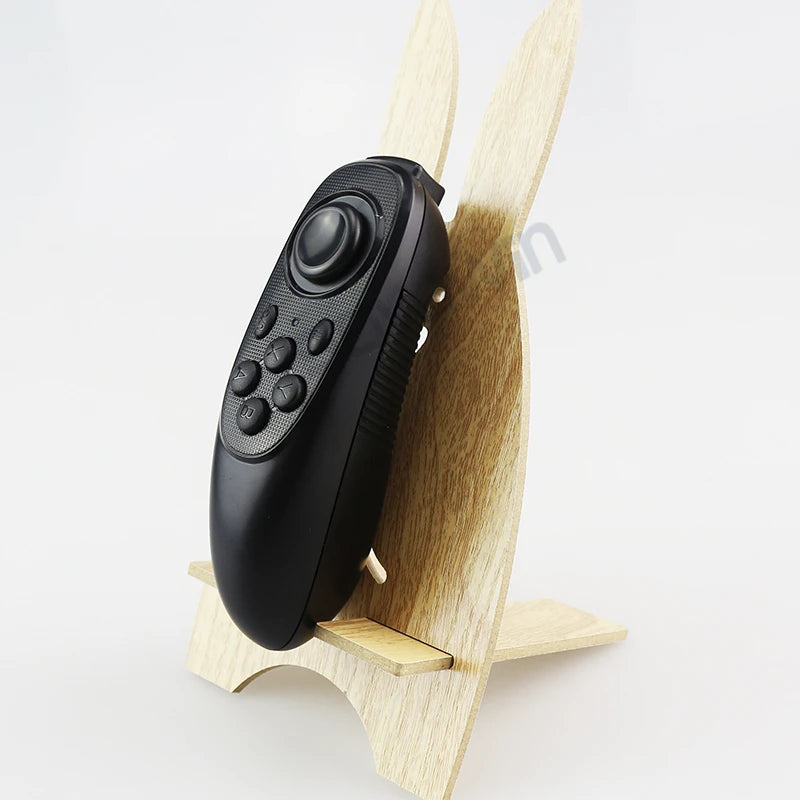 Black wireless VR remote controller with a joystick and buttons, displayed on a wooden rabbit-shaped stand.