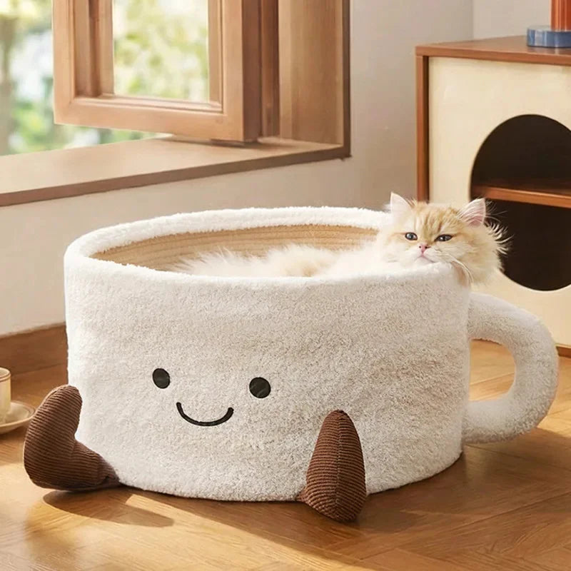 Fluffy white coffee-mug-shaped cat bed with a smiling face, brown feet, and a long-haired cat inside.