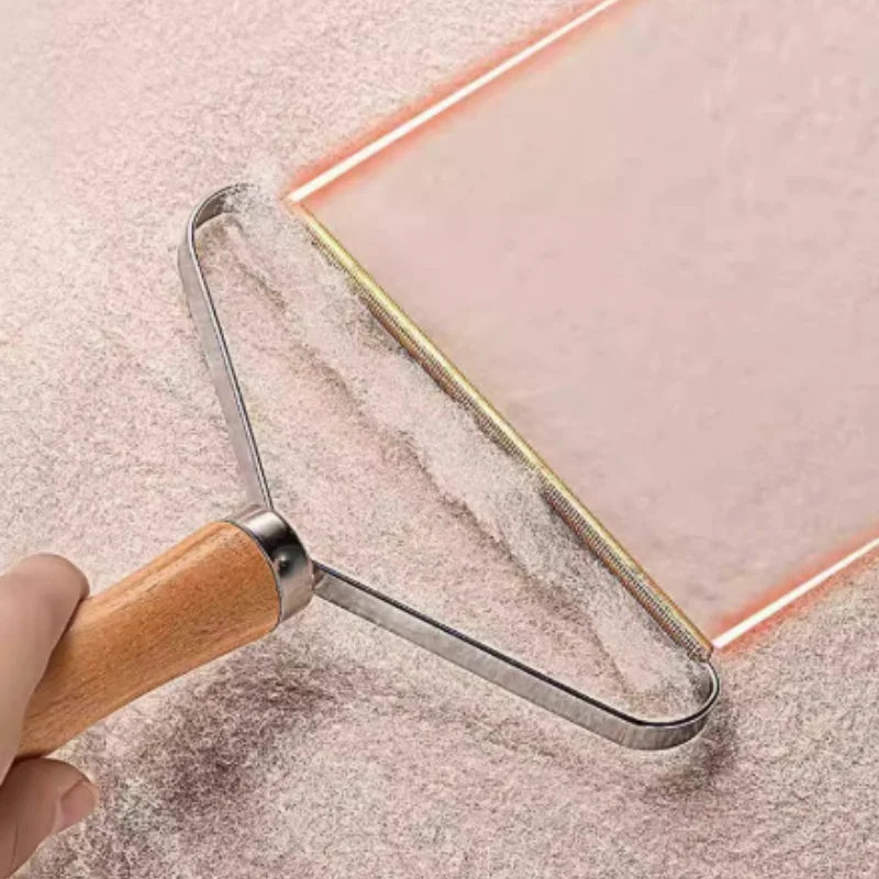 Handheld fabric lint remover with a wooden handle and metal scraper head, cleaning fuzz from a textured pink surface.