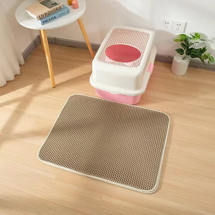 A beige rectangular, double-layered, honeycomb-patterned cat litter mat placed on a wooden floor in front of a litter tray.
