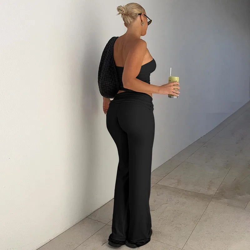Woman wearing a black sleeveless crop top and matching low-rise flared trousers, standing in a hallway.