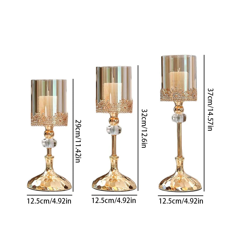 Three gold crystal candle holders in three heights with glass cylinders and white candles.