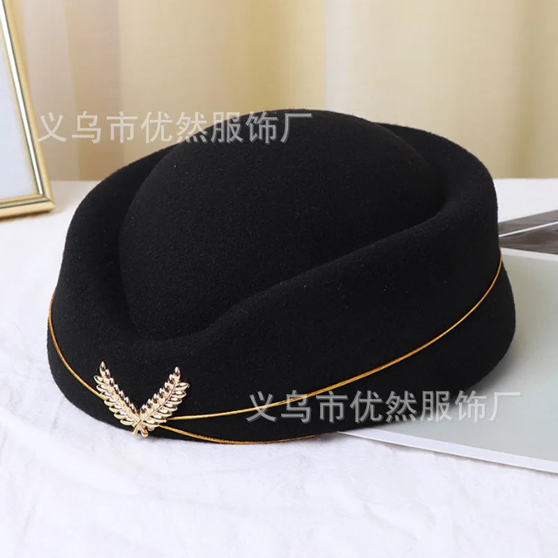 Black vintage-style pillbox stewardess hat with gold trim and a metallic leaf emblem on the front.