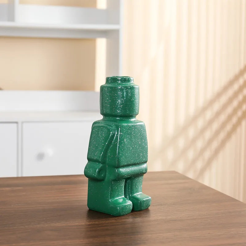 Green speckled robot-shaped decorative ceramic vase standing on a wooden surface.