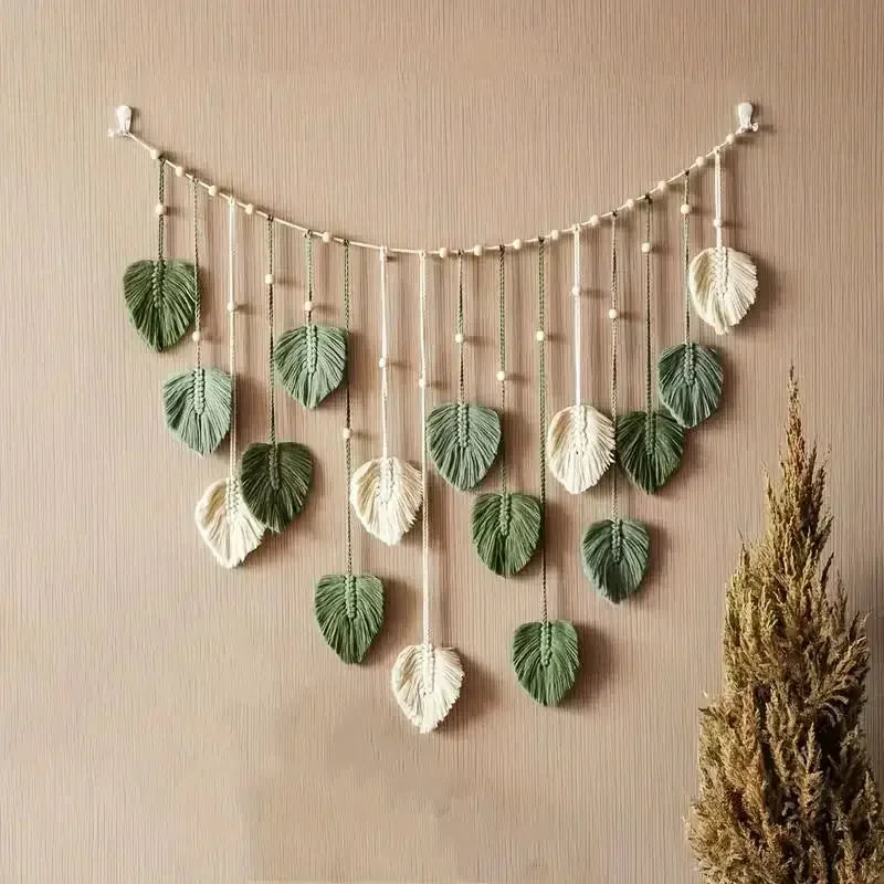 Boho macrame wall hanging featuring sage green and cream leaf-shaped pendants suspended on a beaded string.