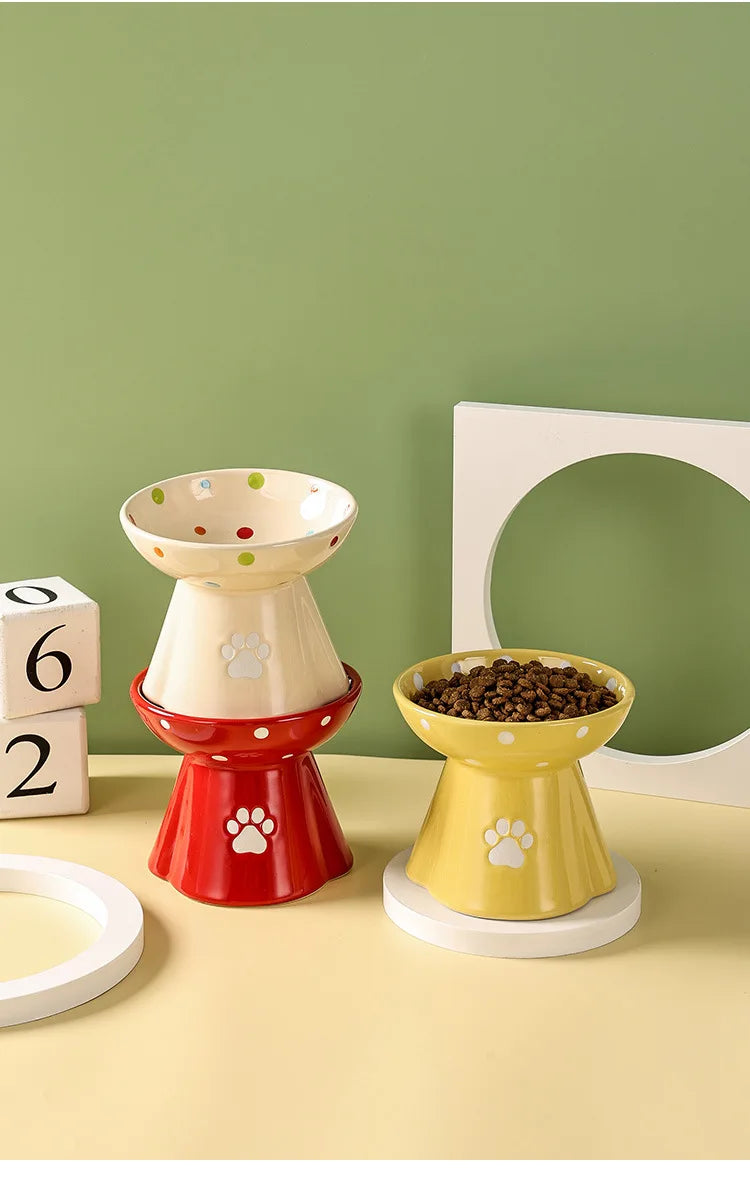Three colourful ceramic elevated cat bowls featuring polka dots and paw print designs.