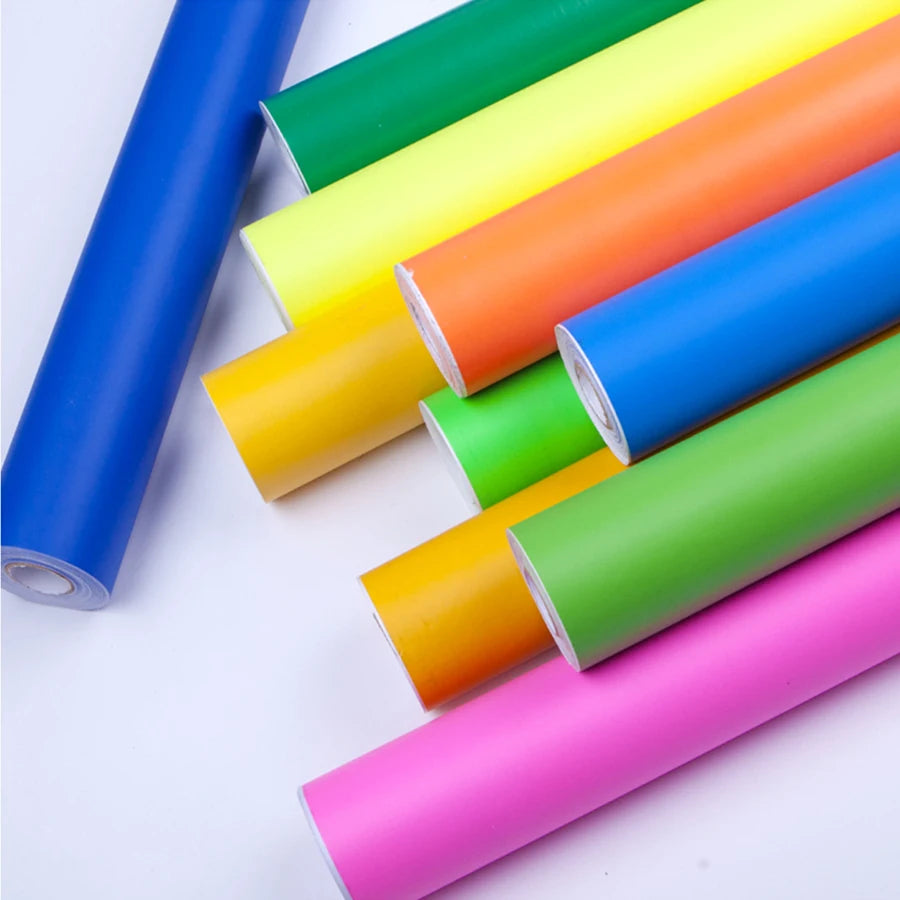 A collection of rolls of vibrant, matte self-adhesive wallpaper in a variety of bright, solid colours.