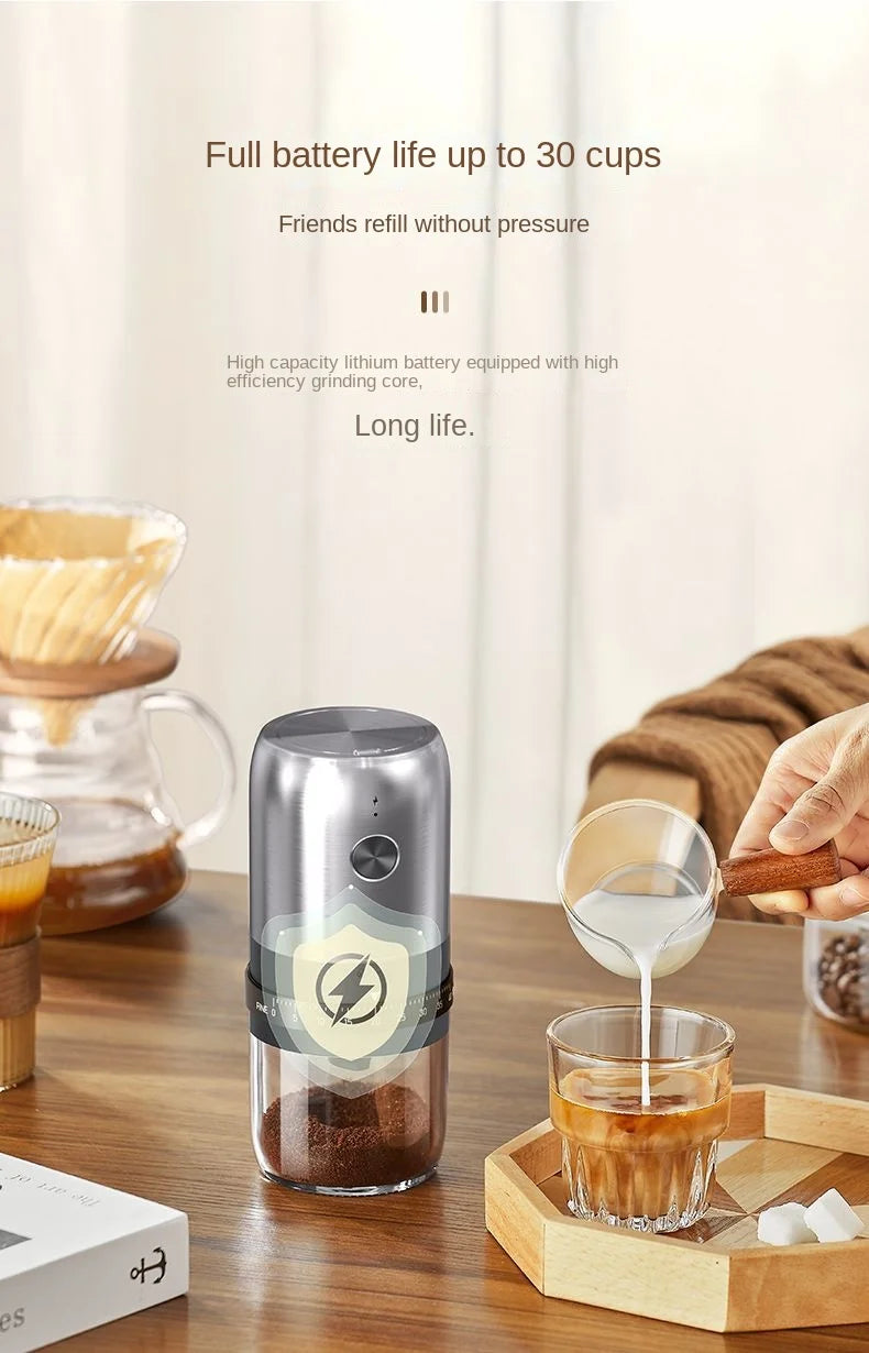 Portable, silver cylindrical electric coffee grinder with a clear base, placed on a wooden table.