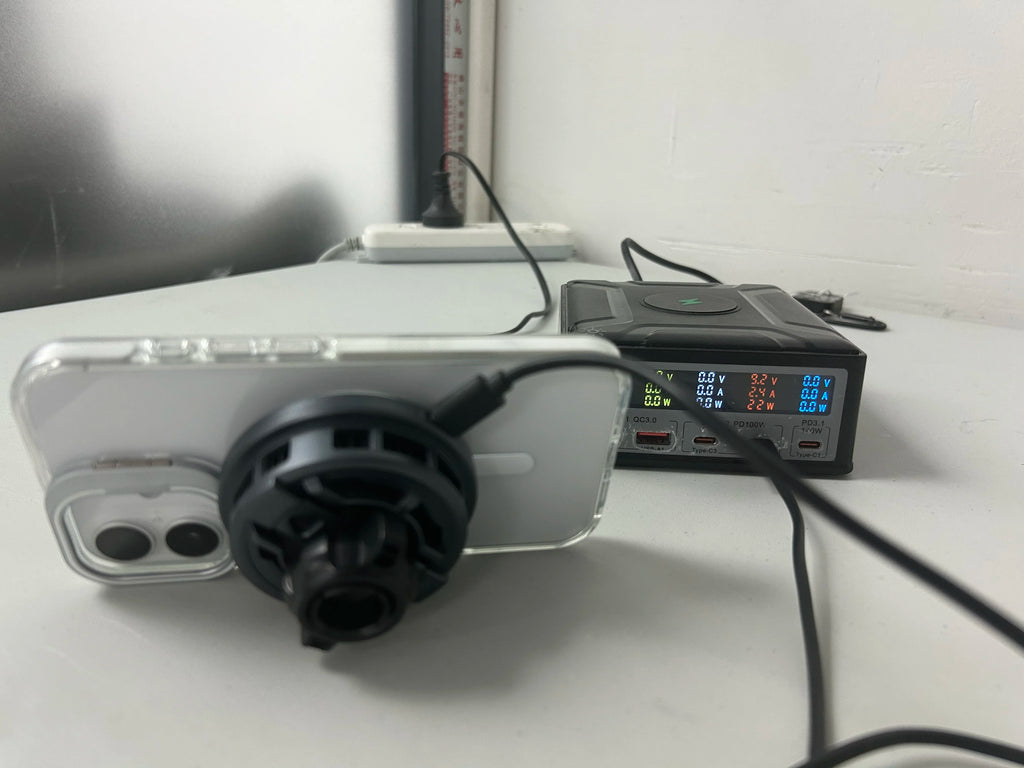 Smartphone with magnetic cooling fan attached, connected to a black digital display charging station on a white desk.