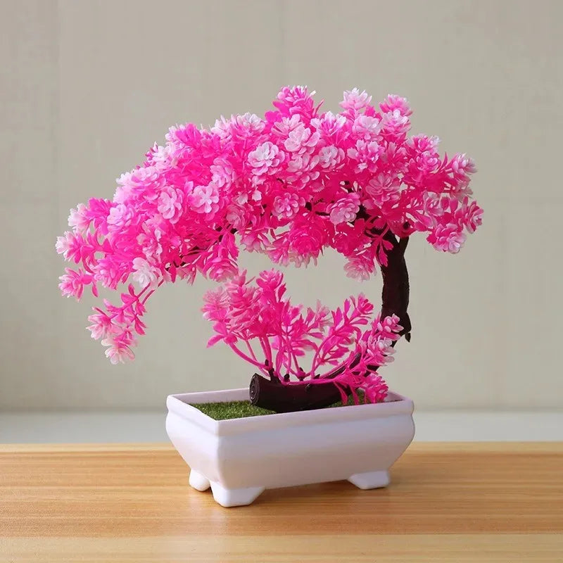 Artificial bonsai tree with bright pink flowers in a white rectangular pot on a wooden surface.