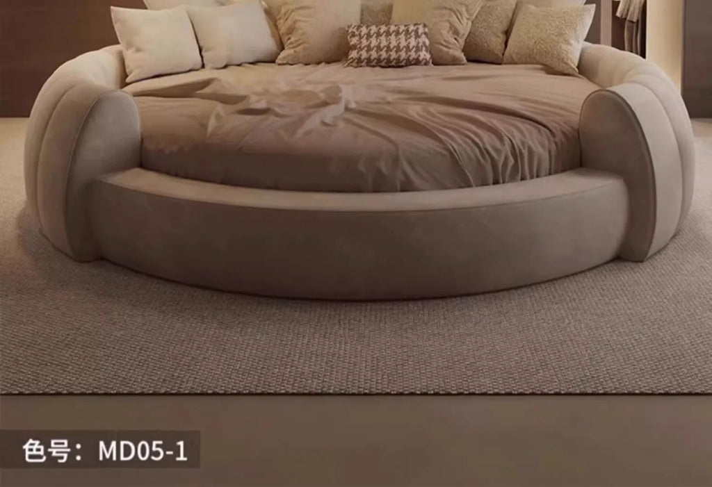 A modern, minimalist circular bed upholstered in soft, beige fabric, styled with neutral cushions.