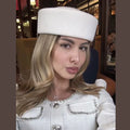 A woman wears an elegant, cream-coloured wool Hepburn-style pillbox hat with a flat top and structured brim.
