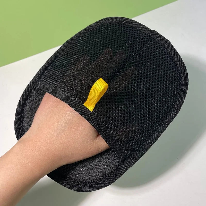 Black mesh exfoliating mitt with a yellow hanging loop, shown being worn on a hand.