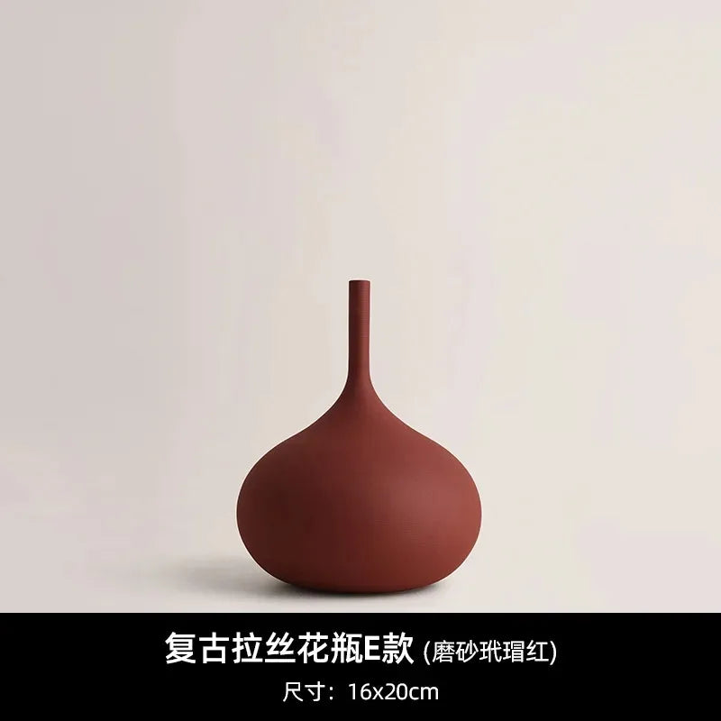 Minimalist dark red ceramic vase with a round base and slender neck, featuring a matte, textured finish.