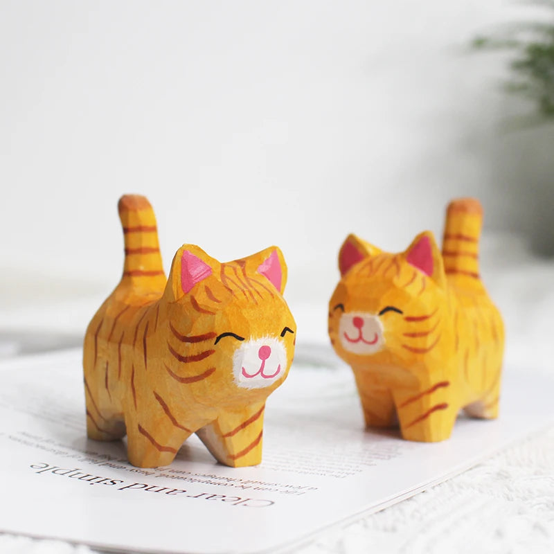 Two charming hand-carved wooden orange tabby cat figurines with painted details, standing on a white surface.