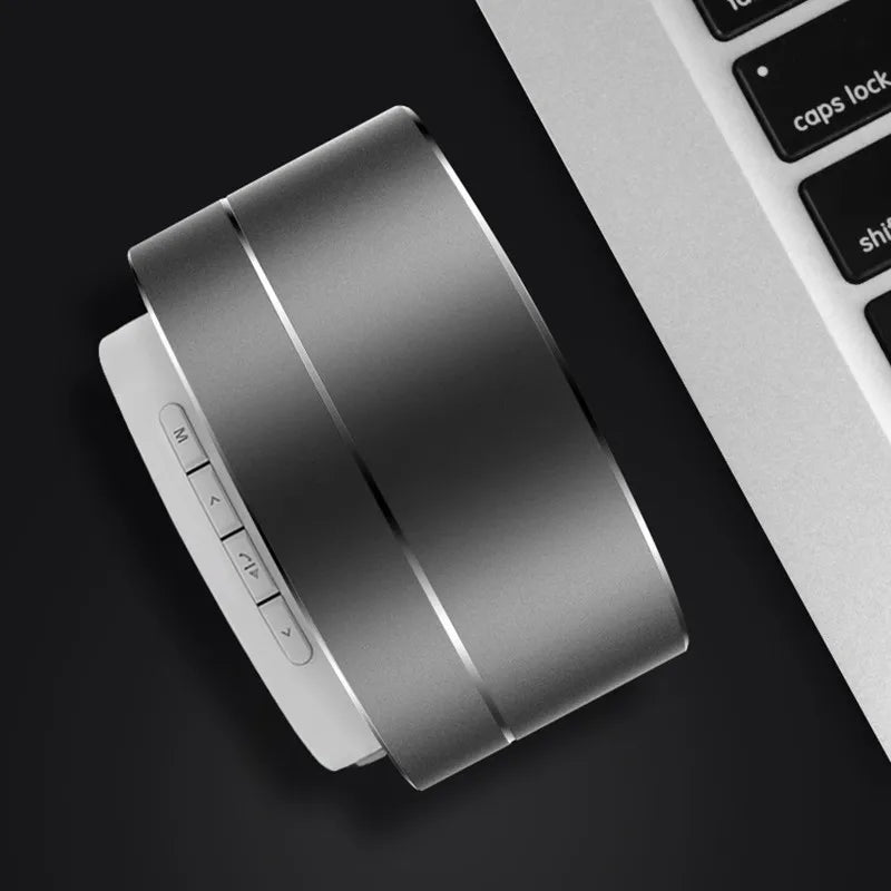 Sleek, grey, portable aluminium Bluetooth speaker with side control buttons, positioned next to a laptop keyboard.