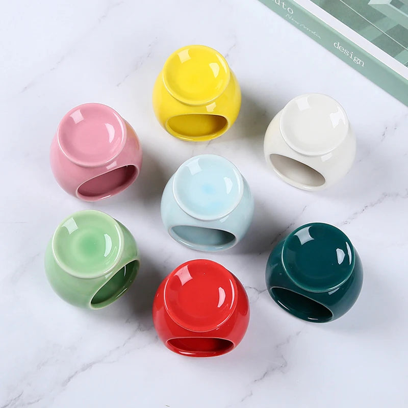 A collection of seven vibrant, round ceramic oil burners in various colours, arranged on a white marble surface.