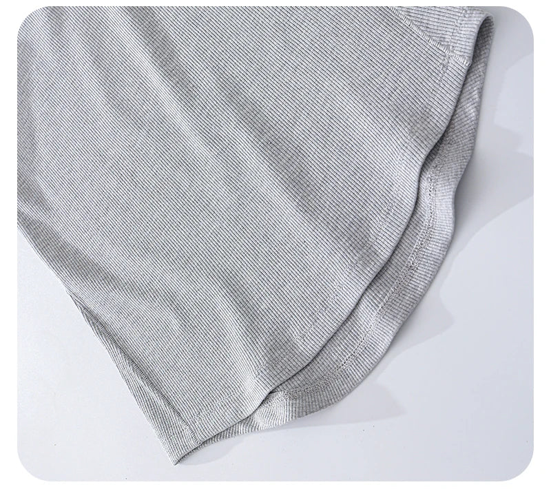 Close-up of a light grey ribbed fabric garment showing a neat, curved hemline with detailed stitching.