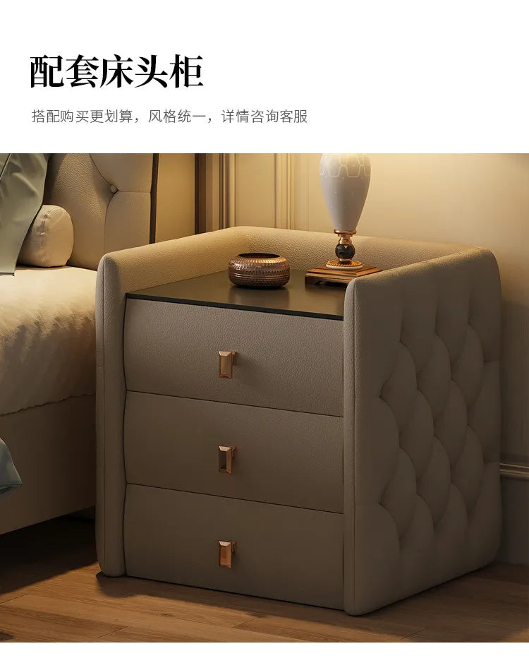 Modern beige upholstered bedside table with three drawers, button-tufted sides, and gold handles.