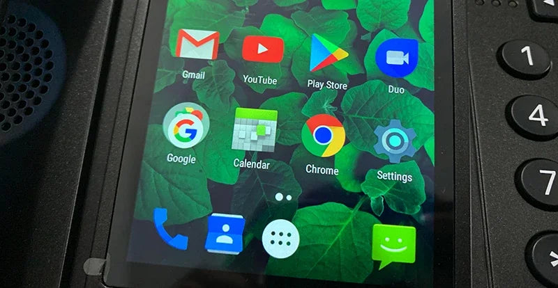 Close-up of a black desk phone with a vibrant, green-leaf patterned touchscreen interface showing app icons.