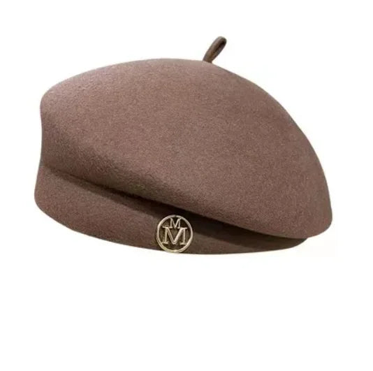 Classic brown wool felt beret with a small stem detail and a gold circular emblem featuring the letter M.