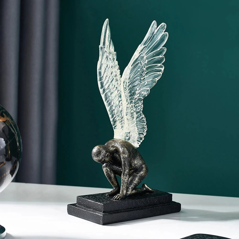 Sculpture of a dark, textured kneeling figure with translucent, uplifted angel wings on a black rectangular base.