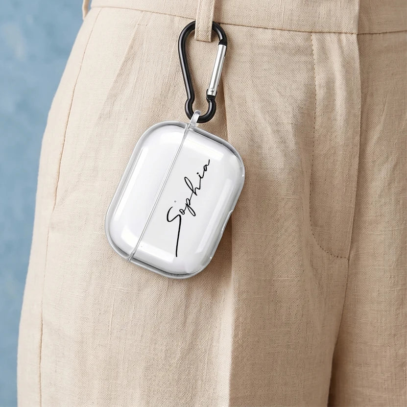 Clear personalised AirPods Pro case with 'Sophia' script, hanging from trousers via a black carabiner clip.