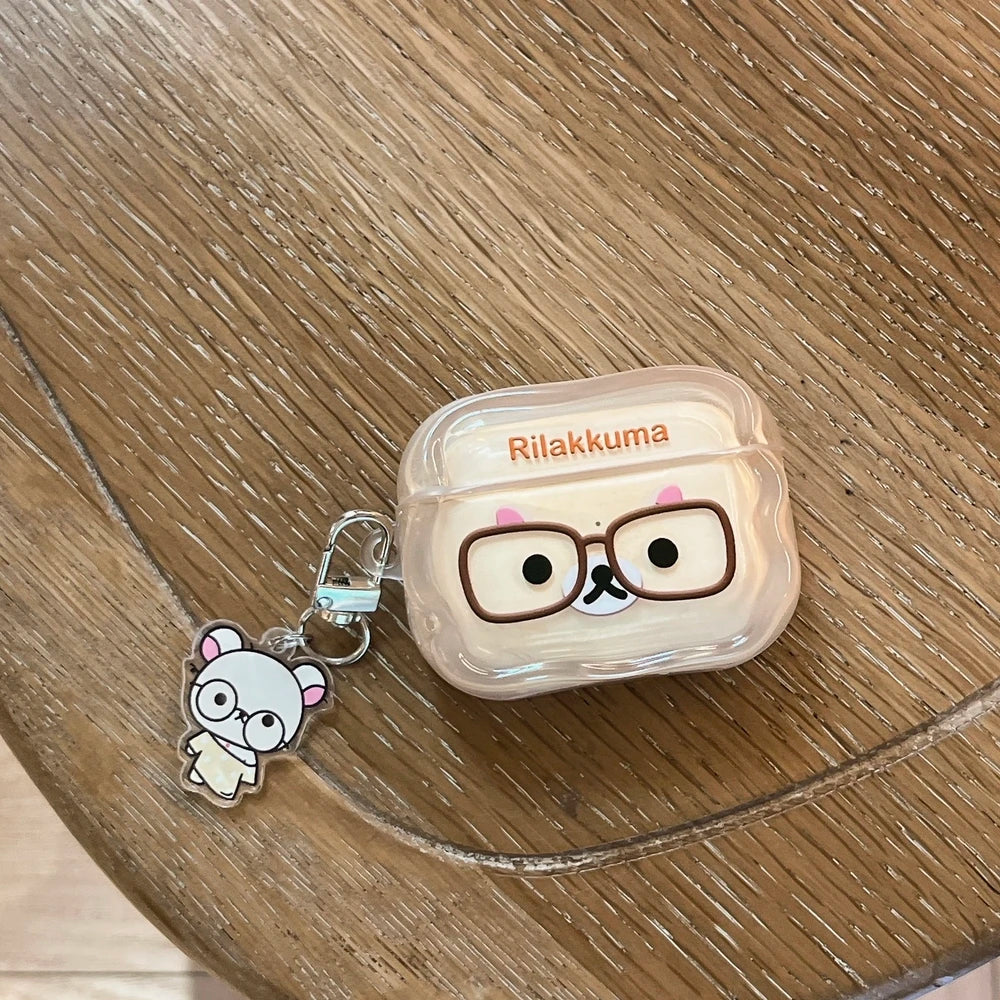 Clear Rilakkuma AirPods case with glasses graphic and matching acrylic charm on a wooden table.
