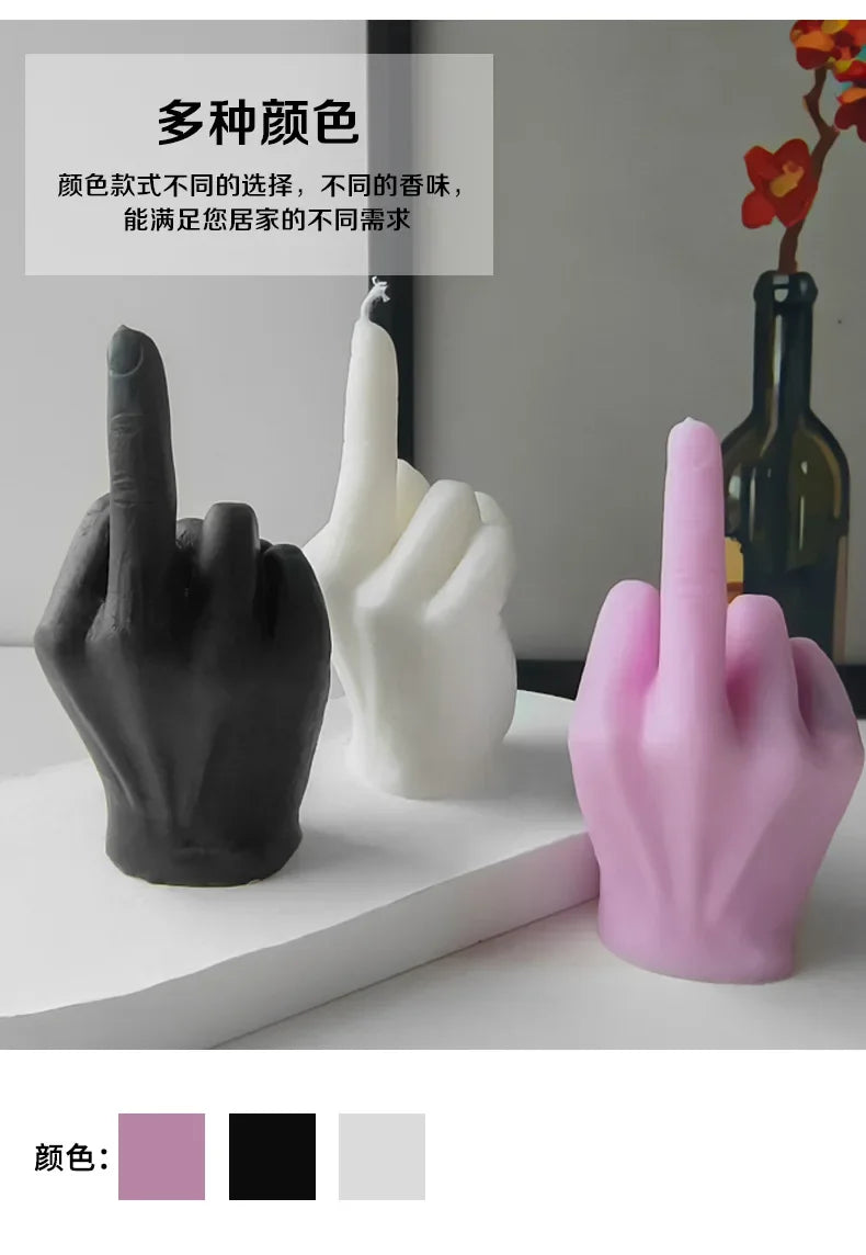 Three hand-shaped wax candles in black, white, and pink, each gesturing with a raised middle finger.