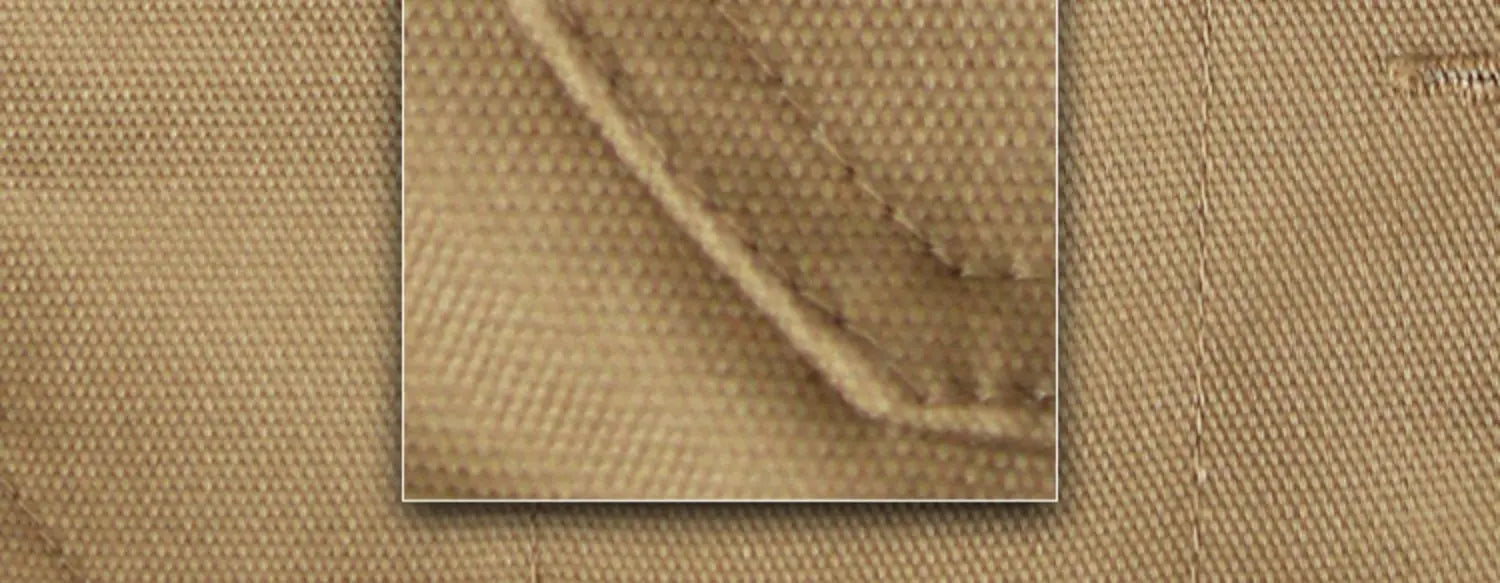 Close-up of durable, tan cotton fabric featuring reinforced stitched seams on these cargo work trousers.