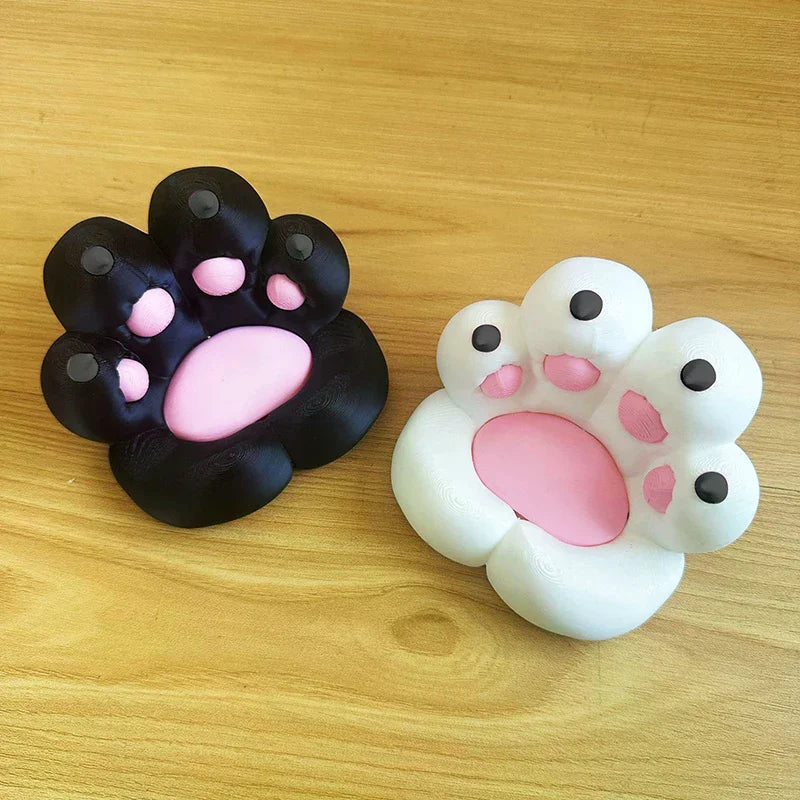 Two 3D-printed cat paw desk accessories in black and white with pink pads, set on a wooden surface.
