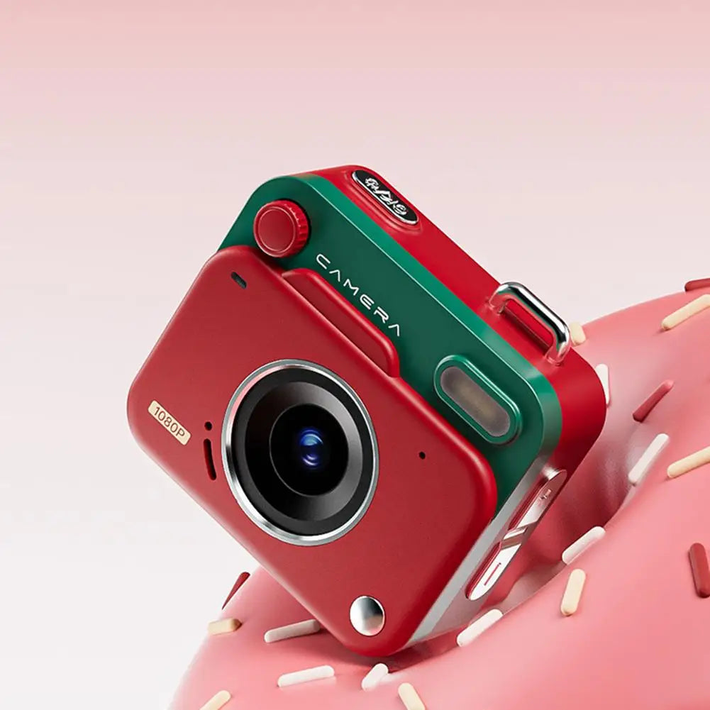 Small red and green plastic digital camera with a 1080p lens, metal accents, and top shutter button on a donut.