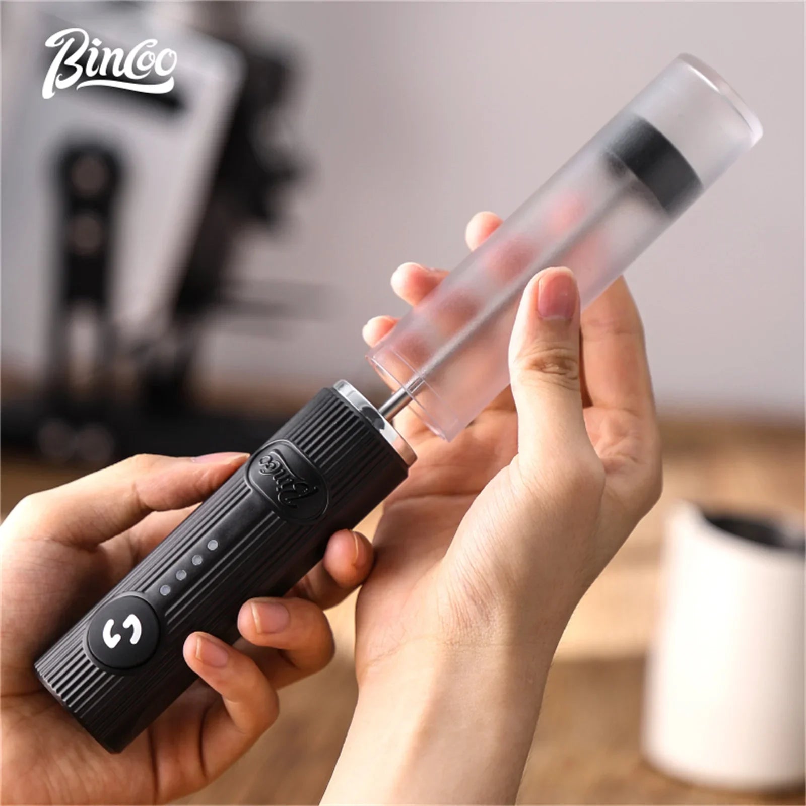 Portable handheld milk frother with a ribbed black motor handle and a detachable clear plastic frothing attachment.