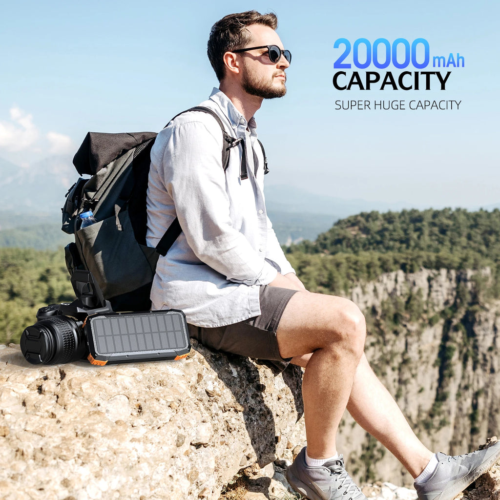 A rugged, black and orange portable solar power bank resting on a rock next to a hiker outdoors.