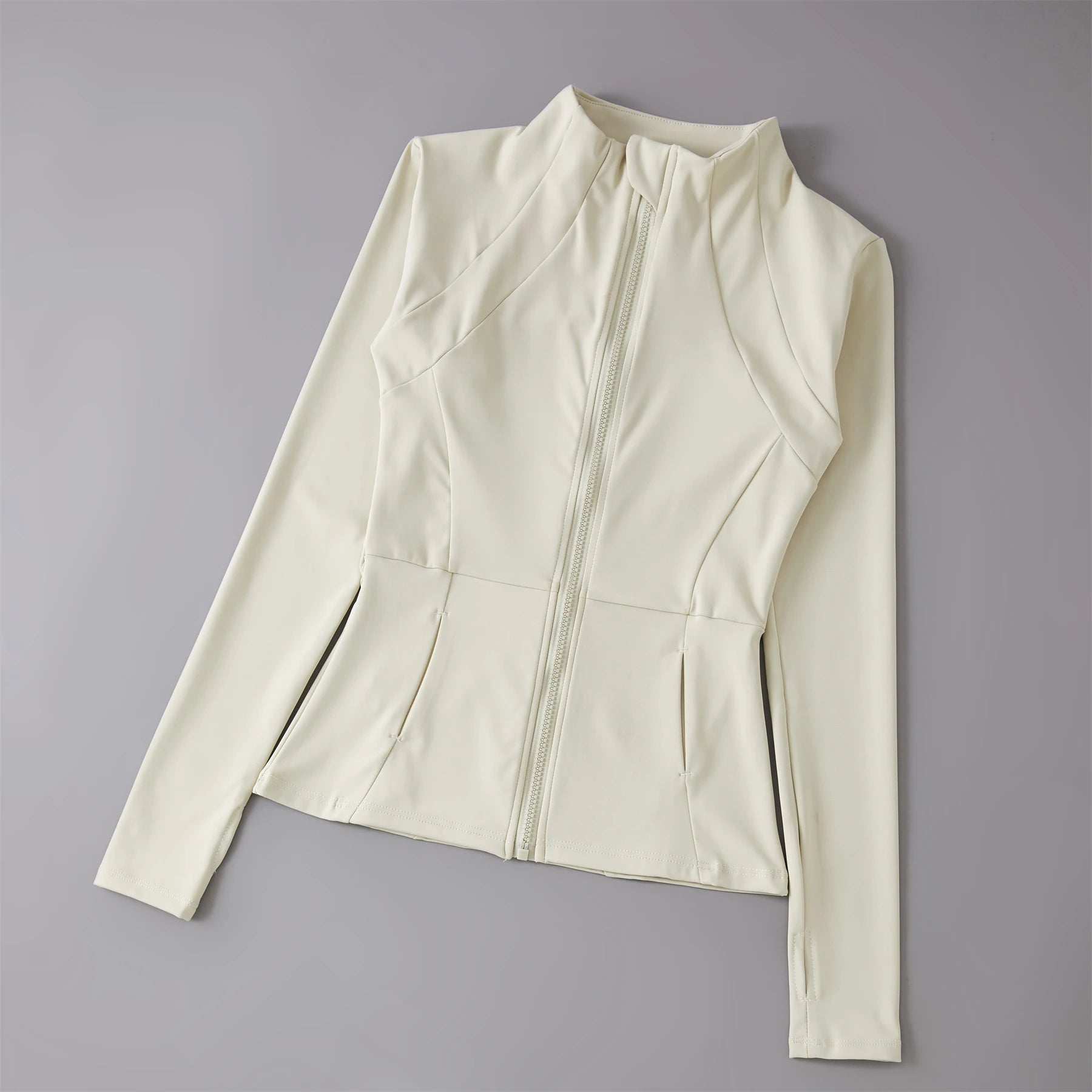 Off-white, fitted zip-up sports jacket with a high neck, panelled detailing, and thumbhole sleeves.