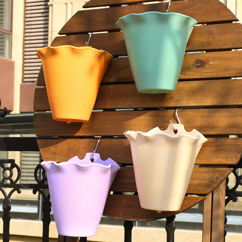Four colorful, scalloped-edge plastic hanging planters in yellow, mint green, purple, and cream on a wooden rack.