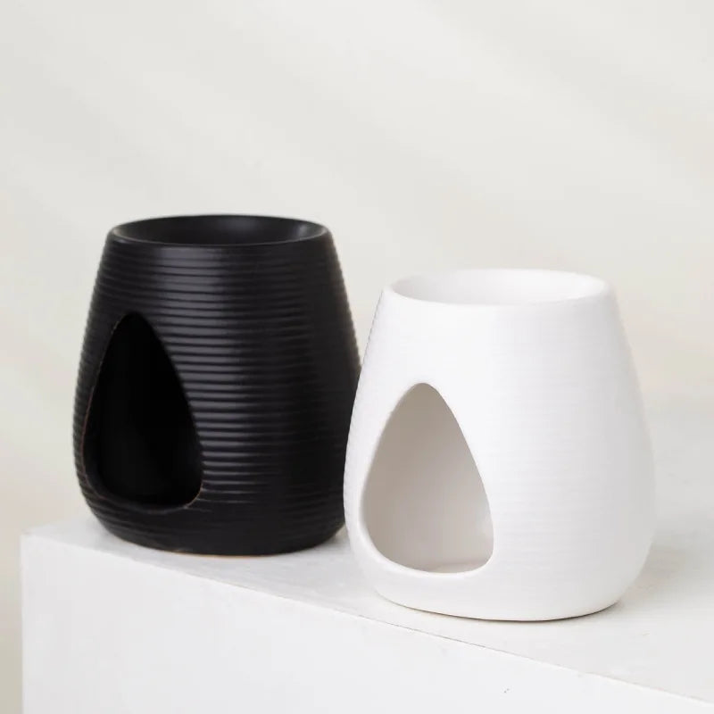 Two minimalist ribbed wax melt burners in matte black and white, featuring a teardrop-shaped opening for a tealight.