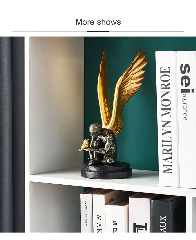 Decorative ornament of a distressed black figure with gold wings, holding a small gold bird, on a black base.